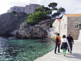岩場と建物がある海沿いを歩く人